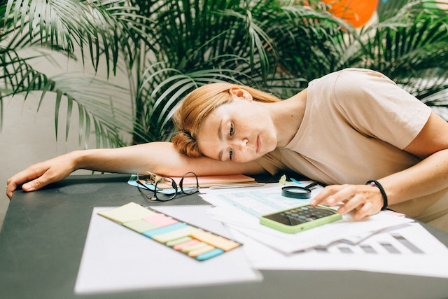 Overwhelmed woman calculating invoices at a desk – struggling with manual billing and paperwork in need of automation.