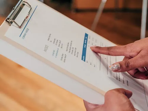 Person reviewing a printed proforma invoice template on a clipboard, showcasing key invoice details used for cost estimation and approval before final sale.