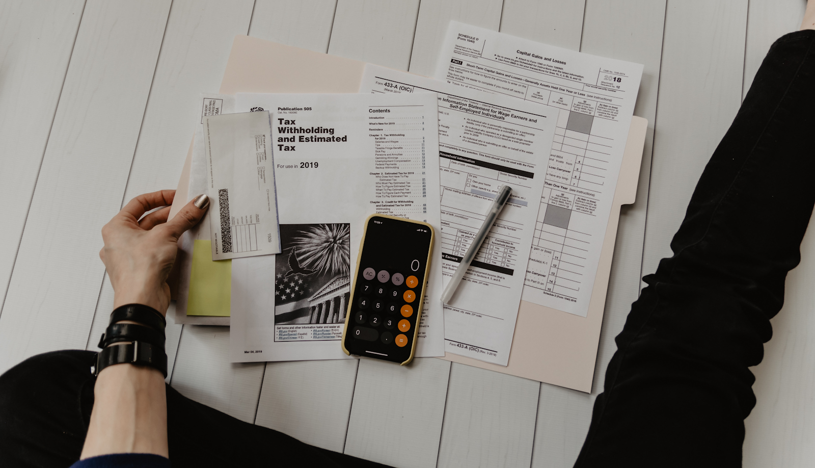 A person doing their taxes at home, surrounded by financial documents, a tax form, a check, and a smartphone calculator — illustrating the difference between invoices and receipts.