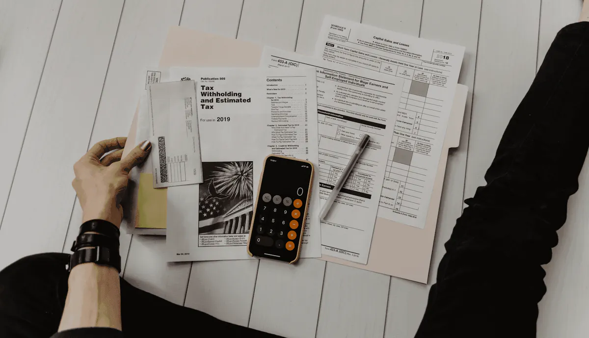 A person doing their taxes at home, surrounded by financial documents, a tax form, a check, and a smartphone calculator, illustrating the difference between invoices and receipts.