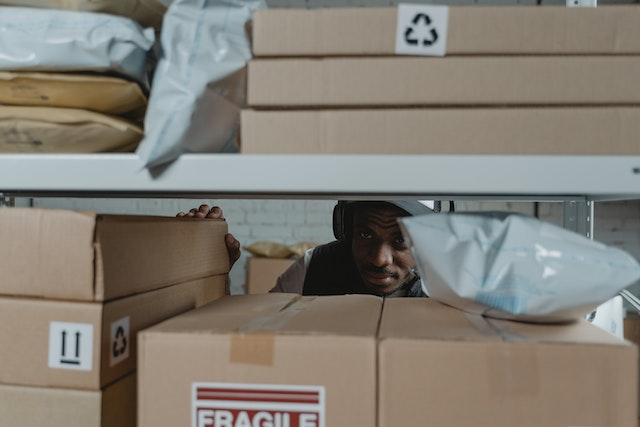 Employee organizing shipping boxes and supplies in a warehouse setting, illustrating inventory management and purchase order system processes.