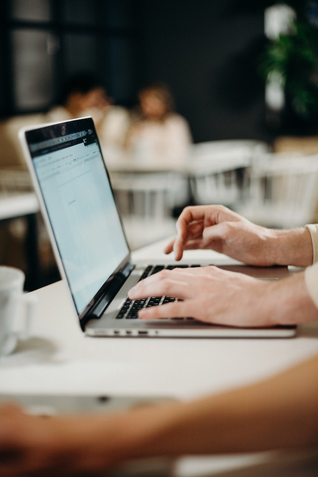 Business professional typing a past due invoice email on a laptop in a cafe, drafting a payment reminder message to clients.