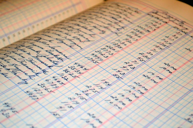 Close-up of a handwritten ledger book page showing a detailed record of invoice numbers and financial entries