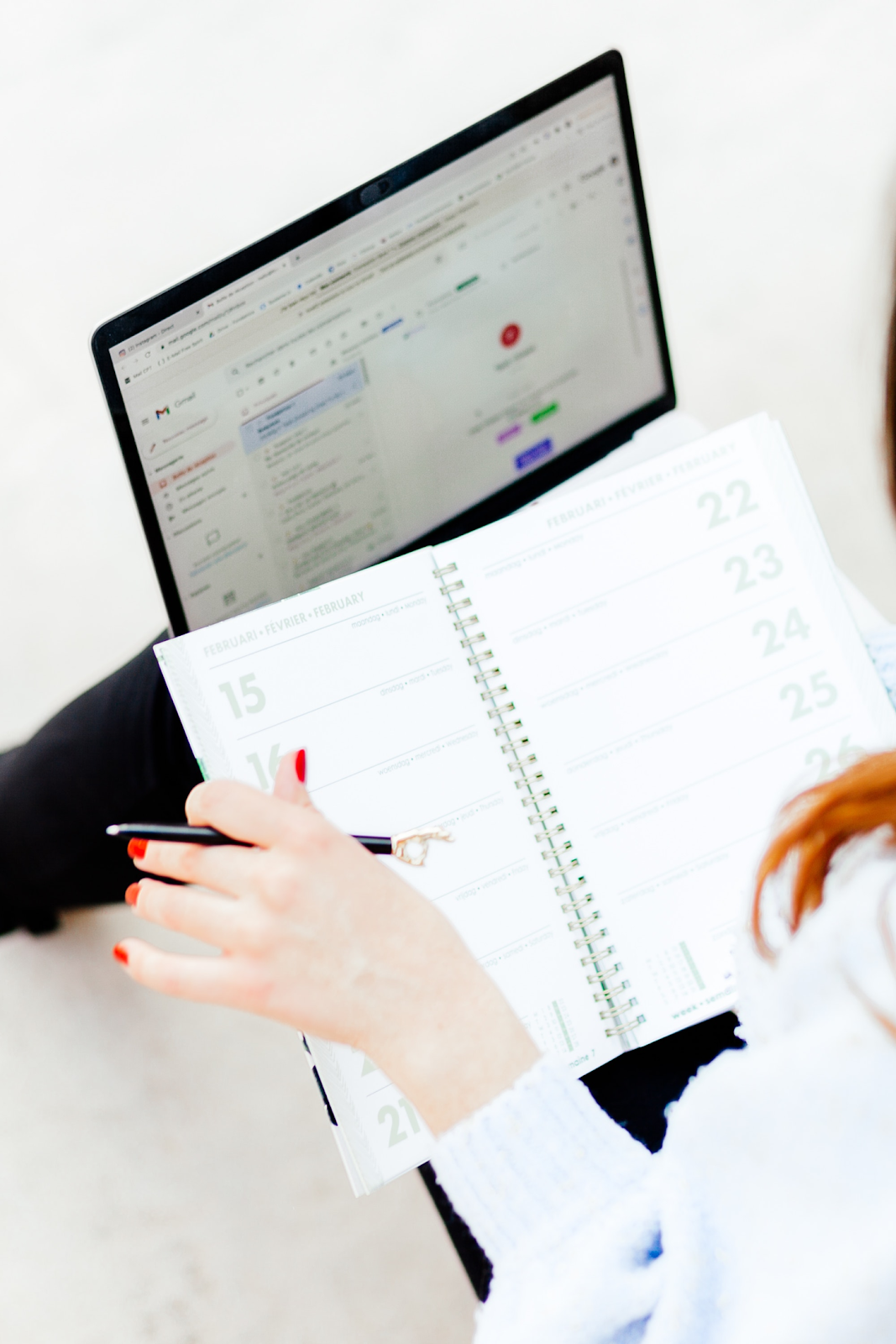 Person reviewing schedule in a planner while composing an invoice email on a laptop – How to write an invoice email with a free template for businesses and freelancers.