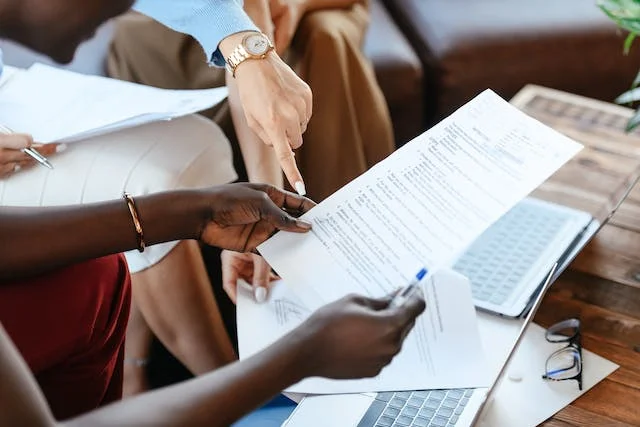 Business professionals reviewing and discussing a printed business contract draft on a laptop during a meeting — step-by-step contract writing process.