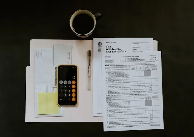 Desk setup featuring a calculator, phone, tax documents, and a cup of coffee, symbolizing the process of facilitating taxation and ensuring compliance with tax withholding and reporting.