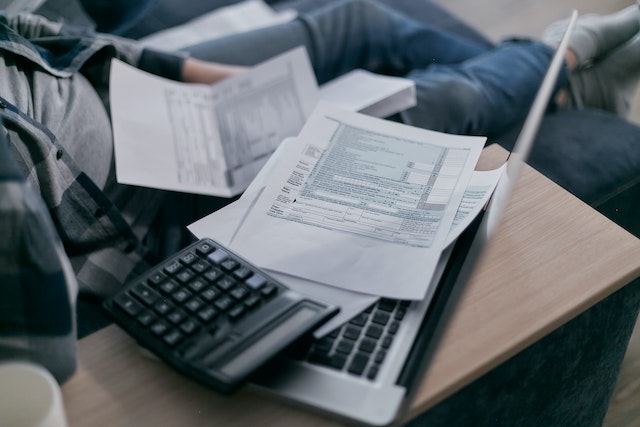 Person reviewing sales invoices and financial documents on a laptop with a calculator and coffee nearby, representing small business accounting and invoice management.