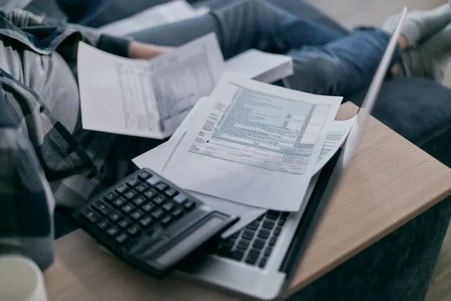 Person reviewing sales invoices and financial documents on a laptop with a calculator and coffee nearby, representing small business accounting and invoice management.