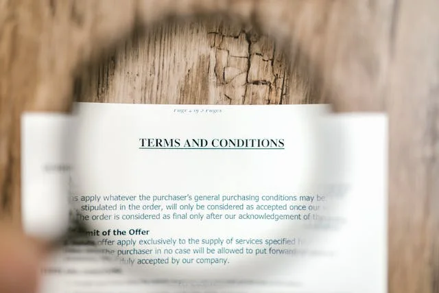 Close-up image of a terms and conditions document, with the text 'TERMS AND CONDITIONS' visible and a magnifying glass focusing on part of the document, highlighting its details.