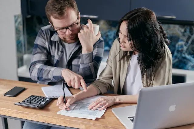 Two professionals reviewing a proforma invoice at a desk with a laptop, calculator, and documents, understanding the purpose and use of proforma invoices in business transactions.