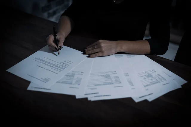 Person signing multiple rental invoice documents on a dark wooden desk, representing automated rental invoice templates for landlords.