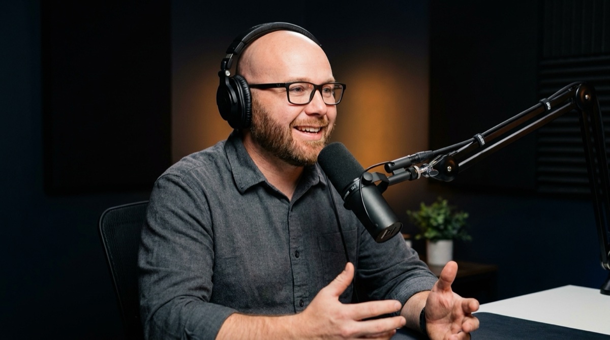 Woody Klemetson on a podcast set, wearing studio headphones and speaking into a Shure SM7B microphone, smiling mid-sentence.